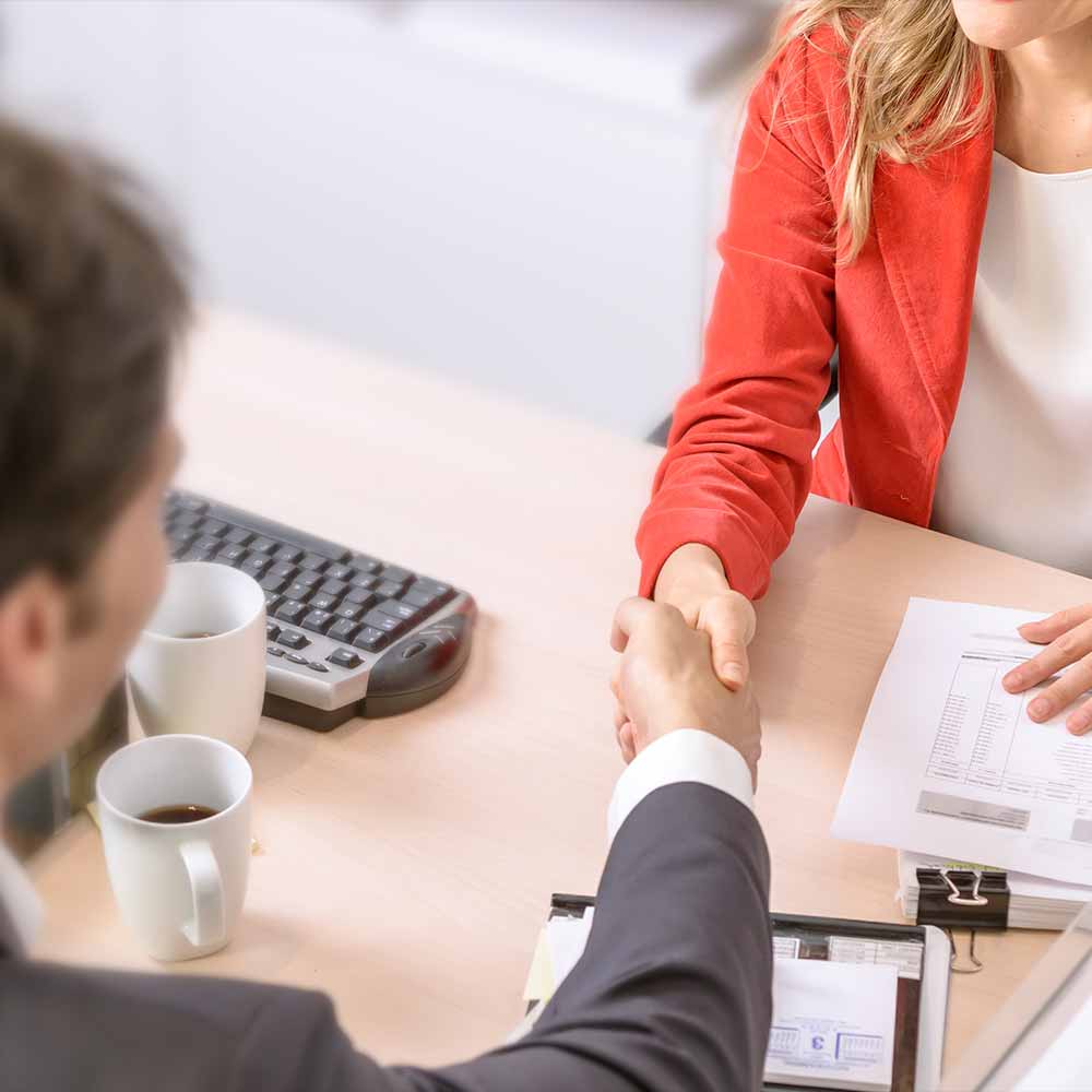 man & woman setting at desk shaking hands